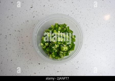 View of coloful diced jalapeno peppers in a plastic container on a kitchen counter, prepped for cooking Stock Photo