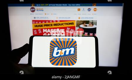 Person holding cellphone with logo of company BM European Value Retail SA on screen in front of business webpage. Focus on phone display. Stock Photo