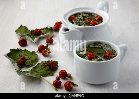 Warming medicinal herbal tea with rose hips and currant leaves on a white wooden table. Flu season Stock Photo