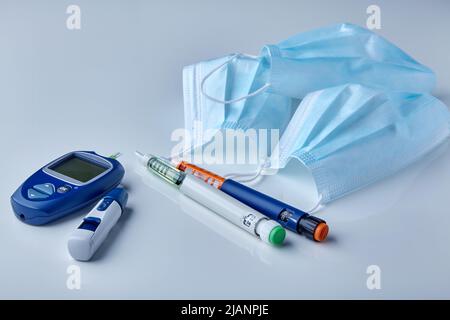 Insulin syringe pens, glucometer and medical masks on a white table. Risk of viral complications in diabetics Stock Photo