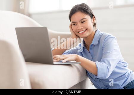 Closeup of smiling asian lady typing on notebook keyboard Stock Photo