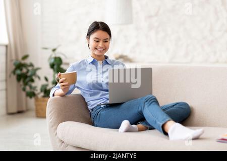 Happy asian woman using computer, drinking tea Stock Photo