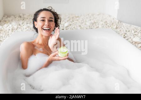 Lovely young woman lying in warm bubble bath, applying cream or face mask, copy space Stock Photo