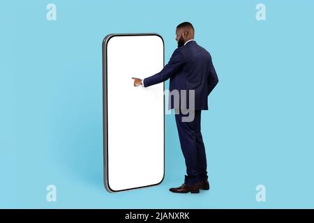 Curious Black Businessman Standing Near Huge Blank Smartphone And Touching White Screen Stock Photo