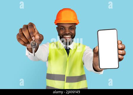 Black Male Civil Engineer In Hardhat Showing Home Keys And Blank Smartphone Stock Photo