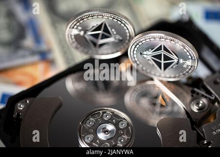 Ethereum coin on hard drive reflecting coins on shiny platter. Euro and dollar banknotes in the background. Storage, mining and exchange of cryptocurr Stock Photo