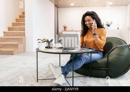 Smiling black woman working and talking on phone at home Stock Photo