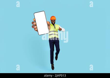 Great Choice. Excited Black Builder Jumping With Blank Smartphone In Hand Stock Photo