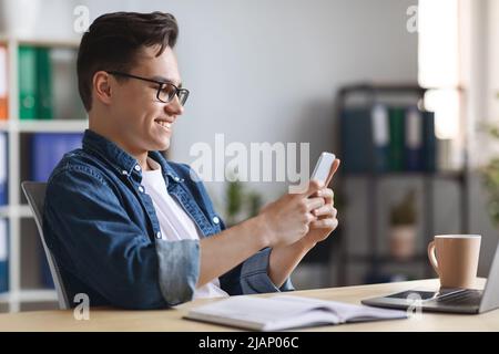 Millennial Businessman Using Smartphone While Sitting At Desk In Office Stock Photo