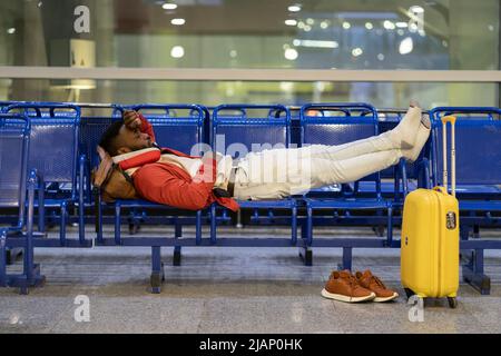 African man napping while waiting for flight. Black guy lying on bench near luggage in airport Stock Photo