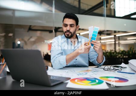 Concentrated young handsome arab man engineer designer with beard shows color palettes in laptop Stock Photo