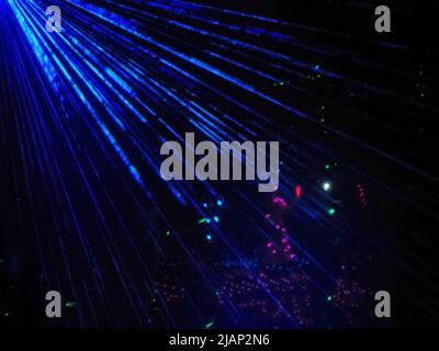 Bright blue neon rays against background of multi-colored lights glowing in the dark. Laser show. Blurred image Stock Photo