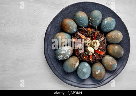 Painted chicken and quail eggs on a dark platter on a white wooden table Stock Photo