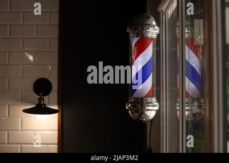 Barber pole spinning at night. International barbershop pole sign. A barber pole calling for people at street. Vintage barbershop. Salon Stock Photo