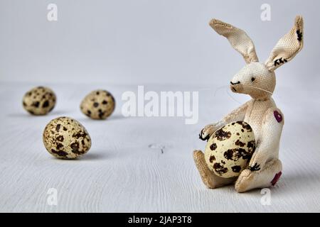 Soft toy hare and quail spotted eggs on a white wooden background. Easter card Stock Photo