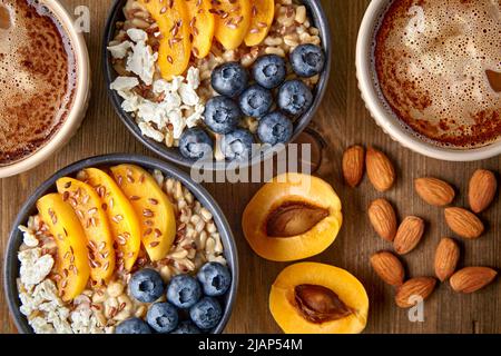 Hearty healthy breakfast for two. Oatmeal with blueberries and apricots, fruits, nuts and coffee Stock Photo