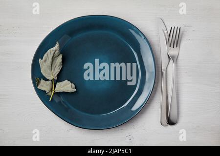 Emerald handmade ceramic plate with cutlery on a white wooden table. Top View Menu Stock Photo