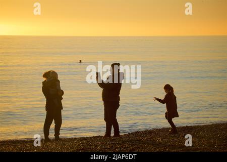 Family on Brighton beach; taking a photograph on a mobile phone.  English channel behind; moody sky. Brighton & Hove, Enghland, UK. Stock Photo