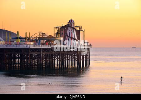 Brighton's Palace Pier, or BRIGHTON PIER.  Brighton & Hove, Sussex, England, UK. Photographed at dusk with the helter skelter and amusements. Paddleboarder int he foreground Stock Photo