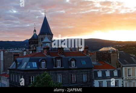 Bell tower of the church in Clermont Ferrand at sunset surrounded by buildings with red roofs Stock Photo