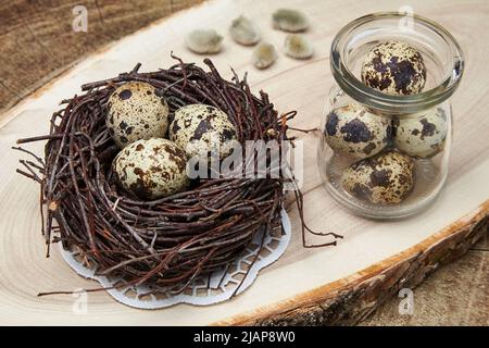 Quail eggs in a nest made of branches and a glass jar with eggs on a natural wood stand Stock Photo