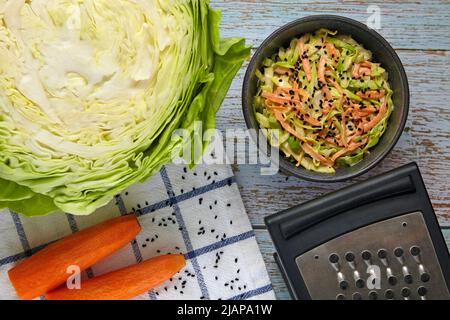 White cabbage and carrot coleslaw salad with black caraway seeds and dressing with mayonnaise and lemon in a black ceramic bowl surrounded by ingredie Stock Photo