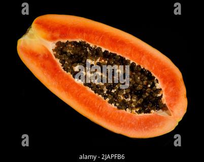 Freshly cut Papaya against black background. The papaya, papaw, or pawpaw is the plant Carica papaya, one of the 22 accepted species in the genus Carica of the family Caricaceae. It was first domesticated in Mesoamerica, within modern-day southern Mexico and Central America. In 2020, India produced 43% of the world supply of papayas. Stock Photo