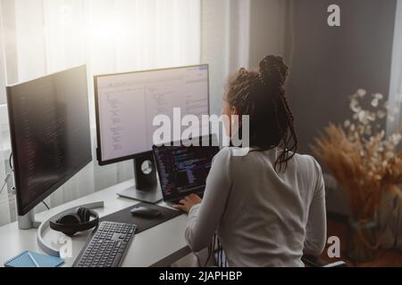 Rear of young woman looking at computer screen while working programming on laptop Stock Photo