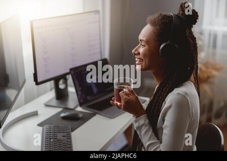 Side view of cheerful young female wearing headphones and programming on computer Stock Photo