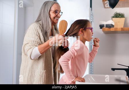 Senior grandmother and granddaughter standing indoors in bathroom, daily routine concept. Stock Photo