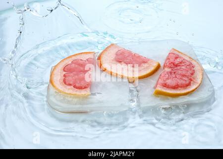 Fresh slices of grapefruit frozen in ice with water splash on white background Stock Photo