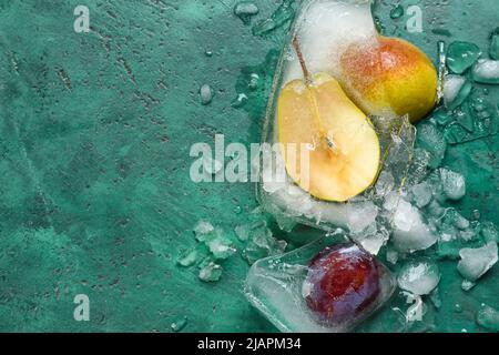 Fresh fruits frozen in ice on green background Stock Photo