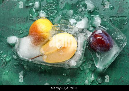 Fresh fruits frozen in ice on green background Stock Photo