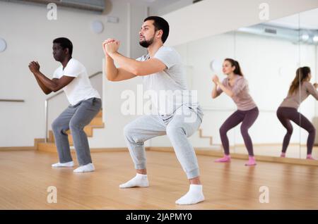 Young man doing squats during warm up before group yoga class Stock Photo