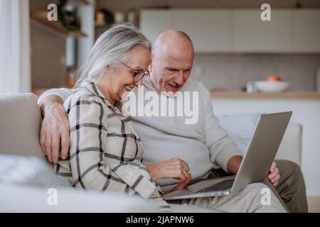 Senior couple sitting on sofa and using laptop together. Stock Photo