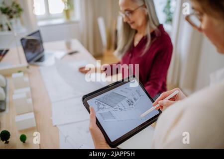 Mature women eco architects with blueprints working on tablet together in office. Stock Photo