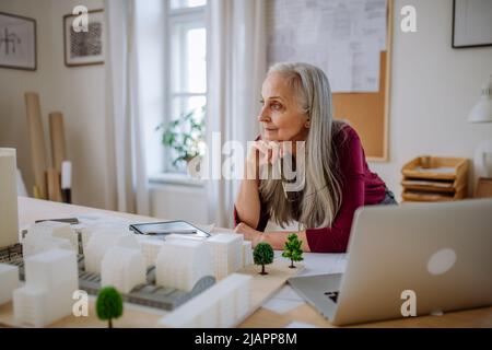 Senior woman eco architect with model of modern bulidings working in office. Stock Photo