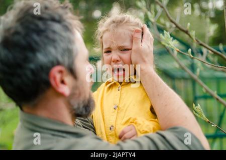 Father holding his crying little daughter and comforting her in garden Stock Photo