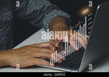 Analysis of business growth trends and company finances Businessman working on laptop with virtual screen graph and chart. arrow pointing to 2022 Stock Photo