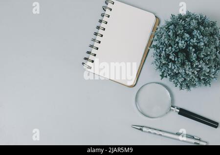 Top view blank notebook and magnifying glass pen on copy space gray background. Stock Photo