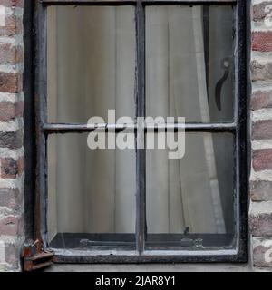 external view of antique casement window in an old red brick building, closed with curtains pulled, square format Stock Photo