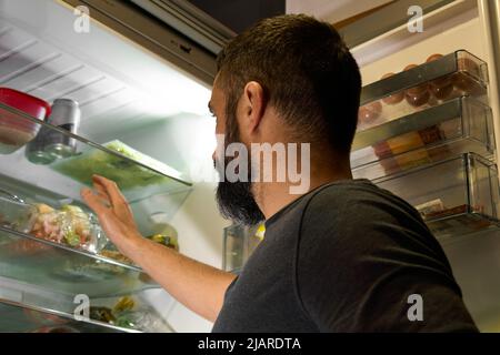 View from the back of a person opening the door of the fridge to catch something inside Stock Photo