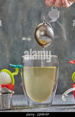 Brews tea in transparent glass with boiling water and tea strainer Stock Photo