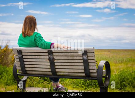 Woman on the bench in sunny day. Back view of a young woman enjoying sunny day in the park. Street photo, copy space for text, selective focus, travel Stock Photo