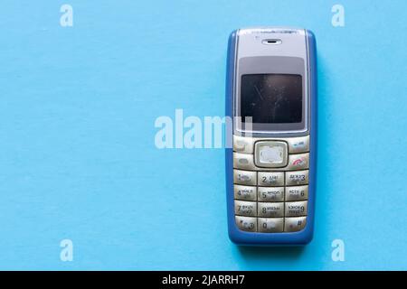 Old blue button mobile phone on blue background. Stock Photo