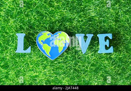 Word LOVE made from wooden letters and a heart shaped world pin on a green grass background. Mother Earth care concept. Stock Photo