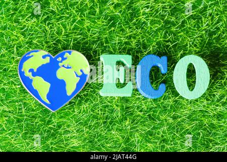 Word ECO made from wooden letters and a heart shaped world pin on a green grass background. Eco green planet concept. Stock Photo
