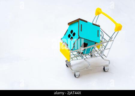 Plywood toy house model in a miniature shopping trolley with copy space. Buying prefab home. Stock Photo