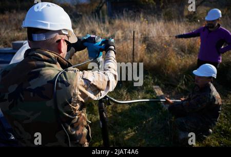 Male workers building pile foundation for wooden frame house. Men builders in white safety helmets drilling piles into the ground.. Stock Photo