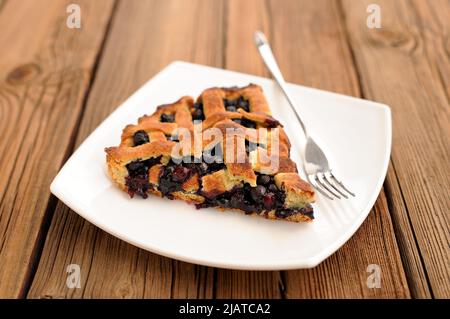 Piece of delicious homemade lattice pie with whole wild blueberries in white plate with fork horizontal Stock Photo